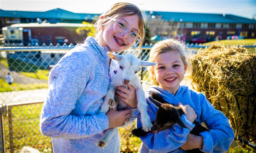 Two girls smile while holding baby goats